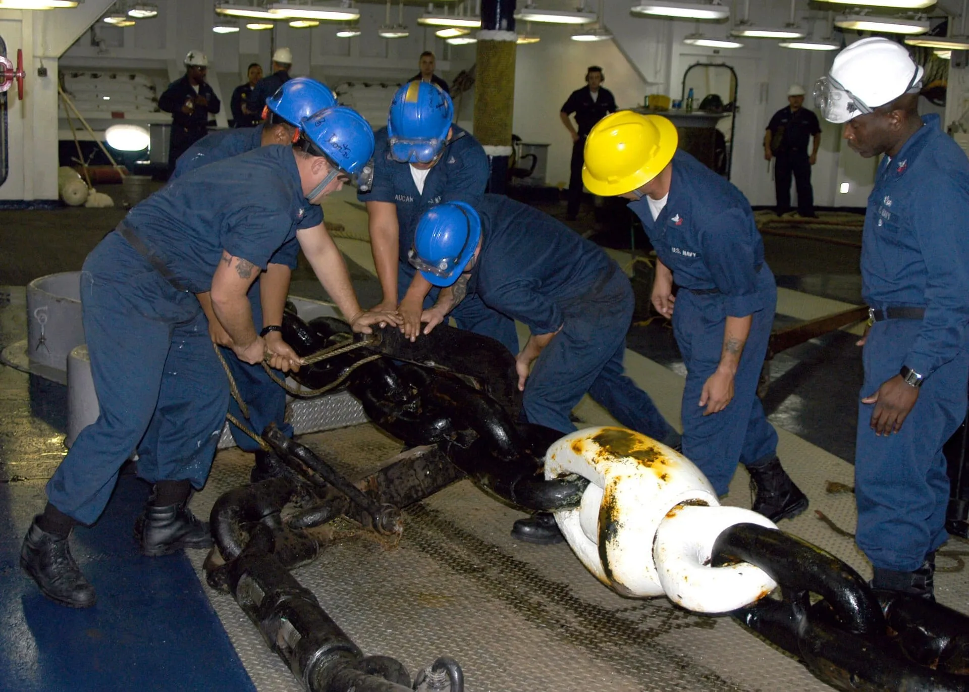 Deck crew in hard hats working together on an anchor chain